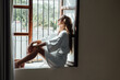 © Berena Alvarez/Stocksy - Young woman in white bathrobe take air at the window