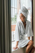© Berena Alvarez/Stocksy - Young woman in white bathrobe take air at the window