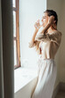 © Berena Alvarez/Stocksy - Woman Drinking Water Near The Window