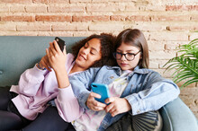 Smiling Teen Girls Using Phones On A Sofa
