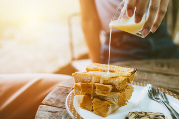 people pouring sweetened condensed milk on top of buttered toast enjoy eating fat and sweet menu in cafe.