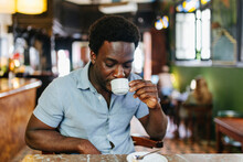 Young Man Drinking Coffee In Colonial Cafe