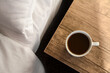 Cup of morning coffee on wooden night stand near bed, top view