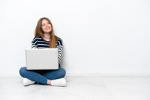 Young Caucasian Woman With A Laptop Sitting On The Floor Isolated On White Background Looking Up While Smiling