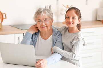 Poster - Little girl with her grandma using laptop in kitchen