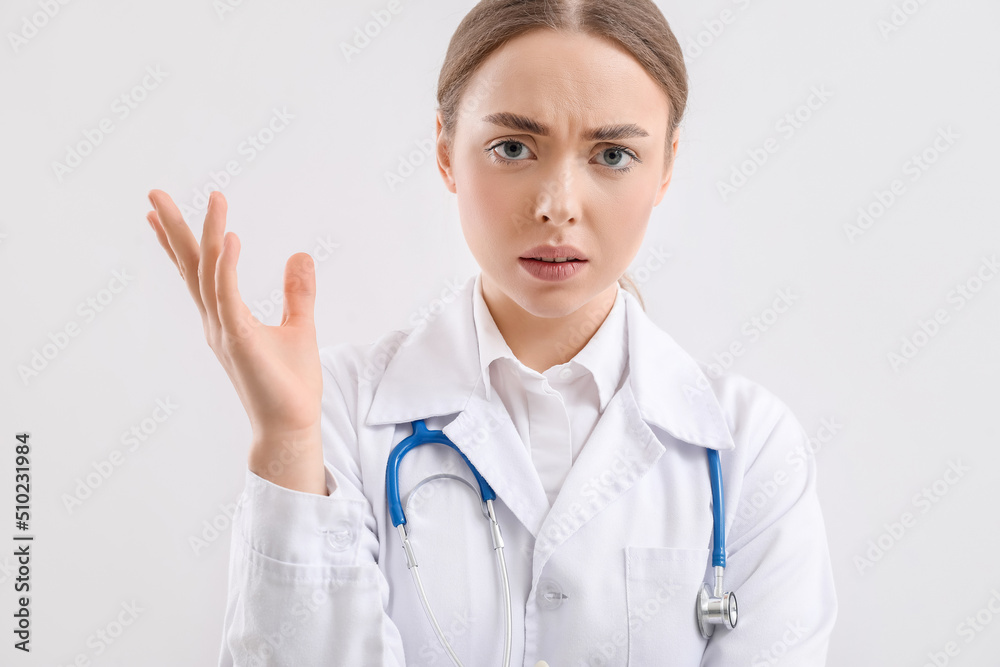 Displeased female doctor on light background