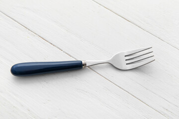 Stylish stainless steel fork on white wooden background