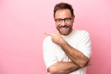 Middle age caucasian man isolated on pink background With glasses and pointing side