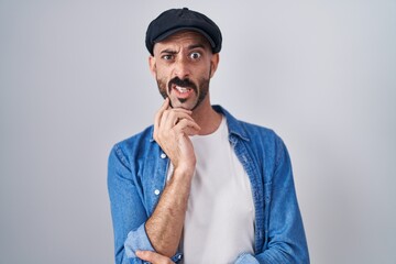 Hispanic man with beard standing over isolated background thinking worried about a question, concerned and nervous with hand on chin