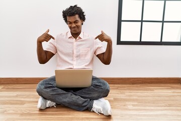 Sticker - African man with curly hair using laptop sitting on the floor looking confident with smile on face, pointing oneself with fingers proud and happy.