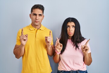 Poster - Young couple standing over isolated background pointing up looking sad and upset, indicating direction with fingers, unhappy and depressed.