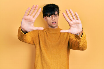 Poster - Handsome hipster young man wearing casual yellow sweater doing frame using hands palms and fingers, camera perspective