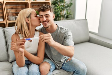 Poster - Young caucasian couple smiling happy holding pregnacy test at home.