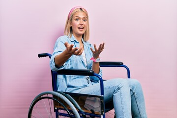 Poster - Beautiful blonde woman sitting on wheelchair smiling cheerful with open arms as friendly welcome, positive and confident greetings