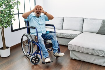 Poster - Handsome senior man sitting on wheelchair at the living room doing ok gesture like binoculars sticking tongue out, eyes looking through fingers. crazy expression.