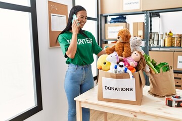 Poster - Young latin woman wearing volunteer uniform talking on the smartphone at charity center