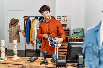 Wall Mural - Young hispanic shopkeeper man smiling happy working at clothing store.