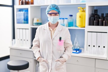 Sticker - Young blonde woman wearing scientist uniform and medical mask standing at laboratory