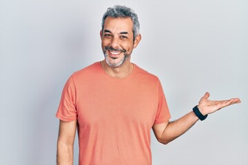 Poster - Handsome middle age man with grey hair wearing casual t shirt smiling cheerful presenting and pointing with palm of hand looking at the camera.