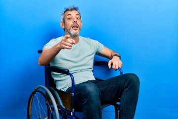 Poster - Handsome middle age man with grey hair sitting on wheelchair pointing displeased and frustrated to the camera, angry and furious with you