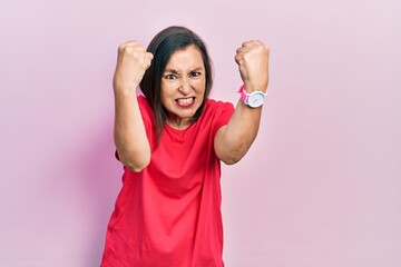 Poster - Middle age hispanic woman wearing casual clothes angry and mad raising fists frustrated and furious while shouting with anger. rage and aggressive concept.