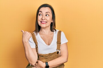 Poster - Middle age hispanic woman wearing casual clothes smiling with happy face looking and pointing to the side with thumb up.