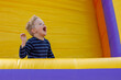Little boy having fun in inflatable castle playground. The child is naughty and shouts loudly. Bright yellow rubber trampoline background, there is free copy space