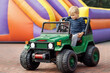 © Linas T - Little child driving green toy car, colored inflatable trampoline in background