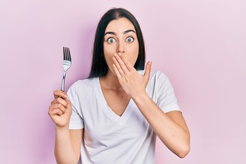 Poster - Beautiful woman with blue eyes holding one silver fork covering mouth with hand, shocked and afraid for mistake. surprised expression