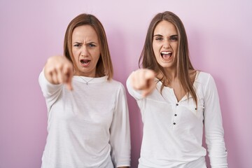 Poster - middle age mother and young daughter standing over pink background pointing displeased and frustrate