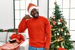 © Krakenimages.com - Young african american man standing by christmas tree smiling doing phone gesture with hand and fingers like talking on the telephone. communicating concepts.