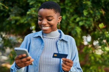 Poster - Young african american woman smiling happy holding smartphone and credit card at the city