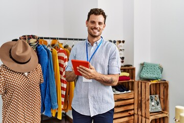 Sticker - Young hispanic shopkeeper man smiling happy using touchpad working at clothing store.