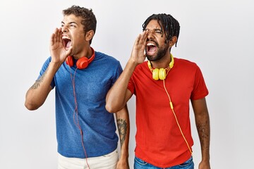 Poster - Young hispanic brothers standing over isolated background wearing headphones shouting and screaming loud to side with hand on mouth. communication concept.