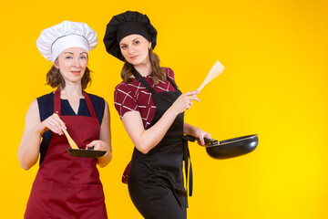 Women in chef's hats. Housewife girls prepare food. Women cooks hold frying pans. Concept of learning cooking. Chefs amateurs on yellow. Adult students of culinary school. 