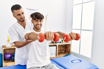 Sticker - Two hispanic men physiotherapist and patient having rehab session using dumbbells at clinic