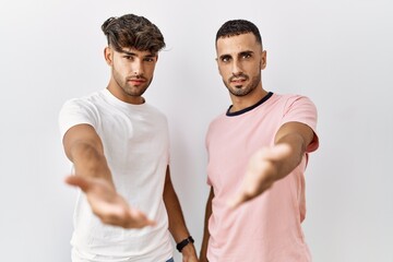 Canvas Print - Young gay couple standing over isolated background smiling cheerful offering palm hand giving assistance and acceptance.