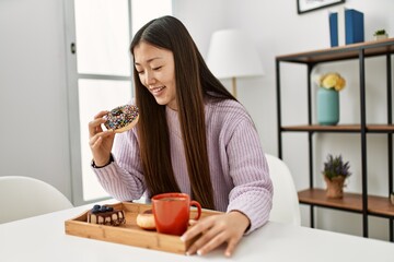 Wall Mural - Young chinese girl having breakfast sitting on the table at home.