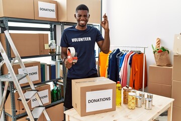 Poster - Young african american volunteer man packing donations box for charity gesturing finger crossed smiling with hope and eyes closed. luck and superstitious concept.