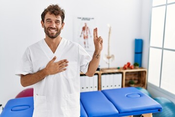 Poster - Young handsome physiotherapist man working at pain recovery clinic smiling swearing with hand on chest and fingers up, making a loyalty promise oath