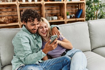 Poster - Young couple using smartphone sitting on the sofa at home.