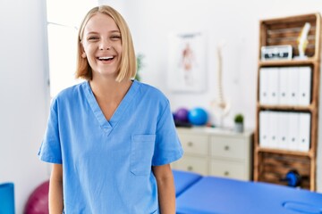 Sticker - Young caucasian physiotherapist woman working at pain recovery clinic looking positive and happy standing and smiling with a confident smile showing teeth