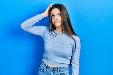 Young brunette teenager wearing casual sweater confuse and wonder about question. uncertain with doubt, thinking with hand on head. pensive concept.