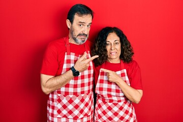 Wall Mural - Middle age couple of hispanic woman and man wearing cook apron pointing aside worried and nervous with forefinger, concerned and surprised expression