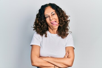 Wall Mural - Middle age hispanic woman with arms crossed gesture sticking tongue out happy with funny expression.