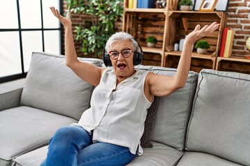 Wall Mural - Senior grey-haired woman listening to music sitting on sofa at home