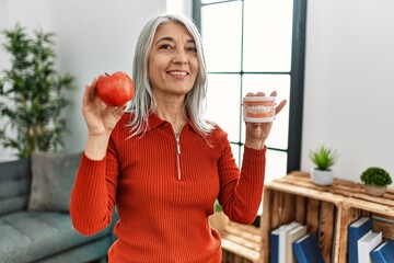 Poster - Middle age grey-haired woman smiling confident holding red apple and denture at home