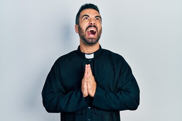 Poster - Handsome hispanic priest man with beard standing over isolated background angry and mad screaming frustrated and furious, shouting with anger looking up.