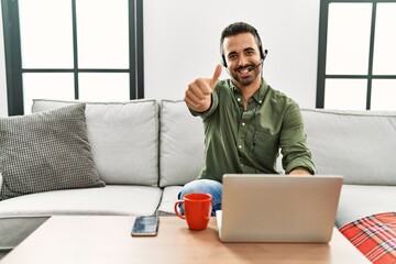 Poster - Young hispanic man with beard wearing call center agent headset working from home approving doing positive gesture with hand, thumbs up smiling and happy for success. winner gesture.