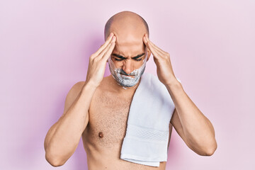 Canvas Print - Young bald man shirtless shaving beard with foam suffering from headache desperate and stressed because pain and migraine. hands on head.